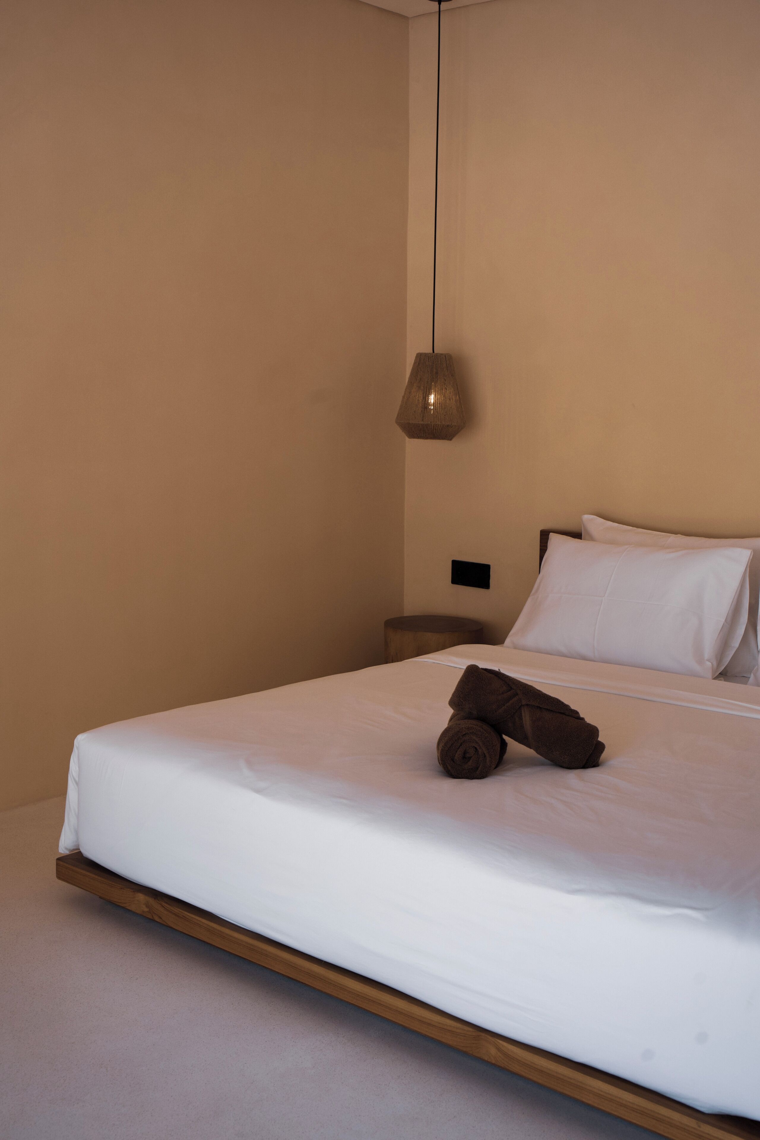 A neatly made bed with a wooden headboard, a single bedside table, and a hanging lamp.