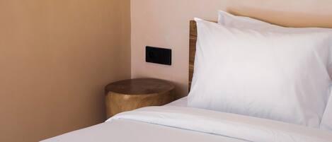 A neatly made bed with white linens, a brown towel, and a wooden nightstand with a lamp.