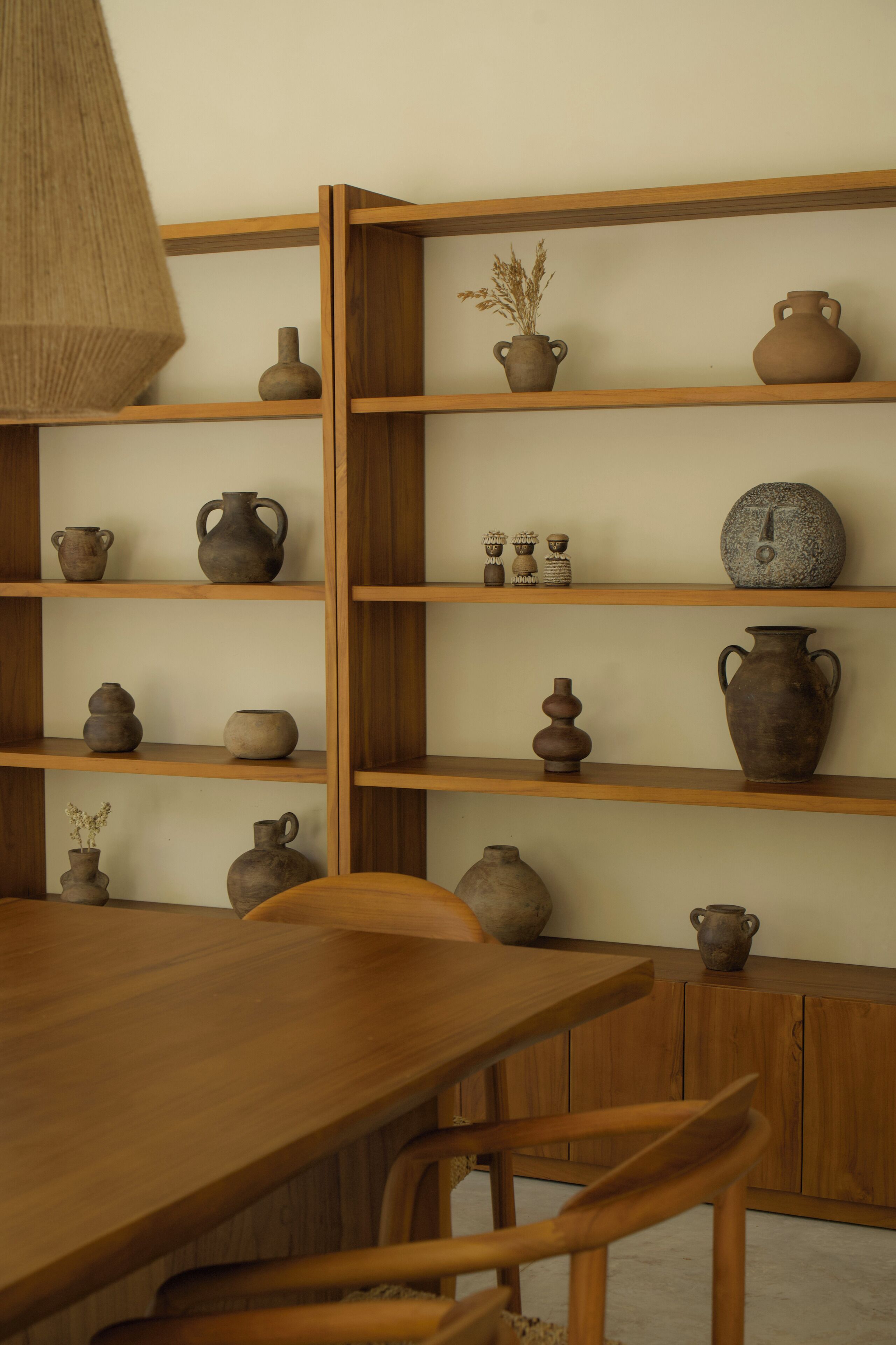 A wooden dining table with chairs, surrounded by shelves with various pottery items.