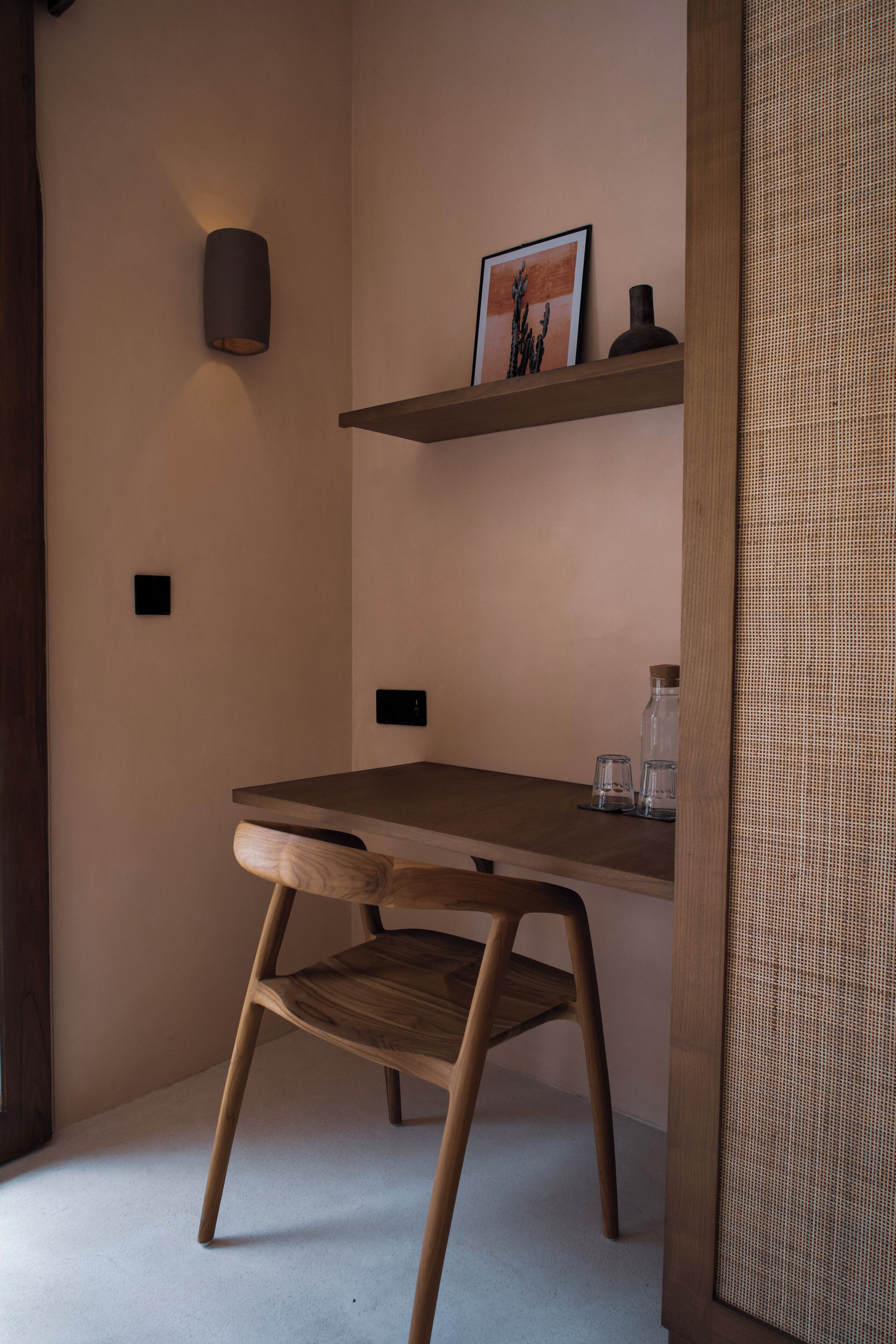 Quarto com escrivaninha de madeira, uma cadeira, prateleira com uma imagem e painel de parede texturizado.