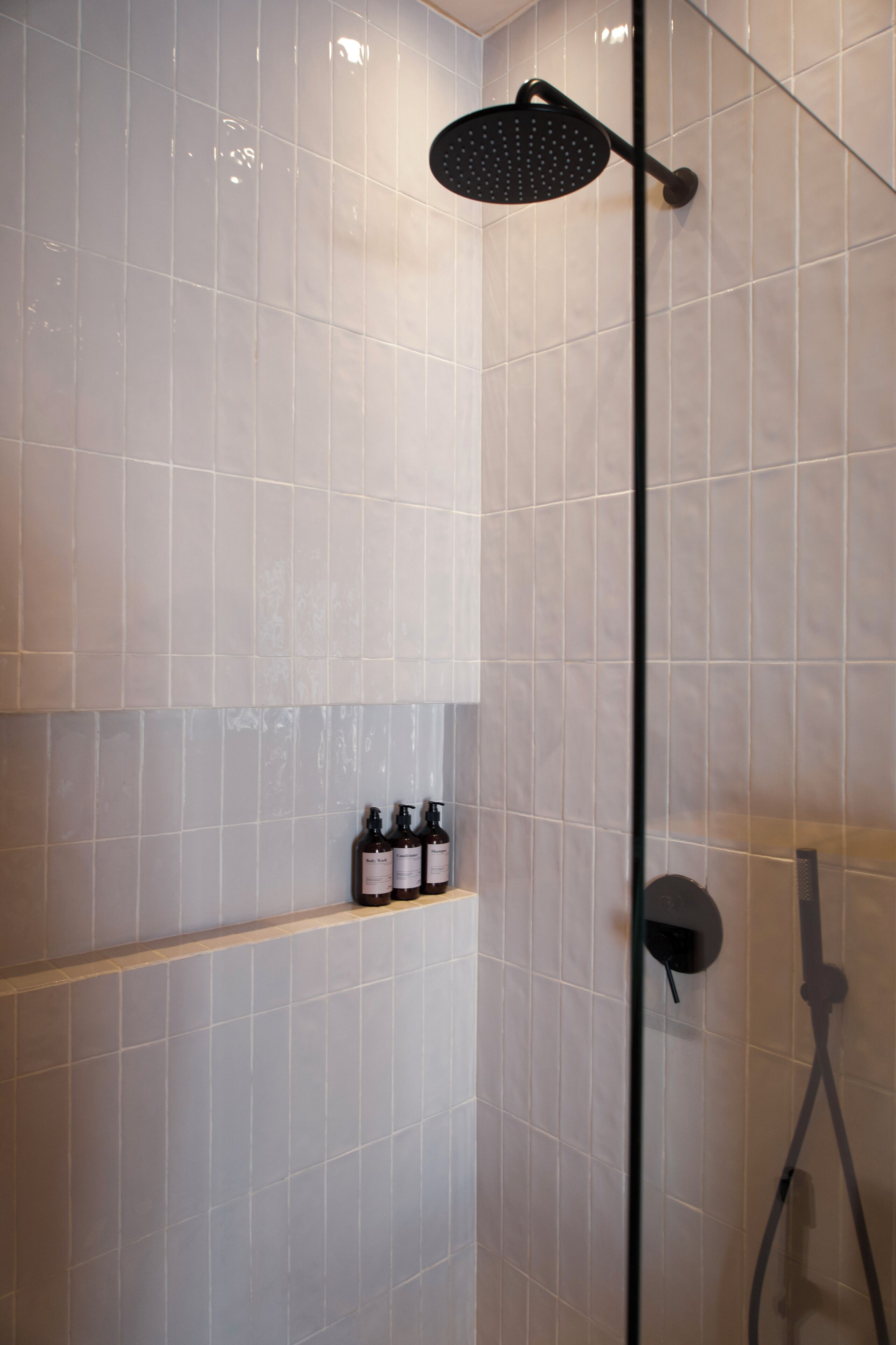 A shower with a handheld showerhead, a glass partition, and a shelf with bottles.