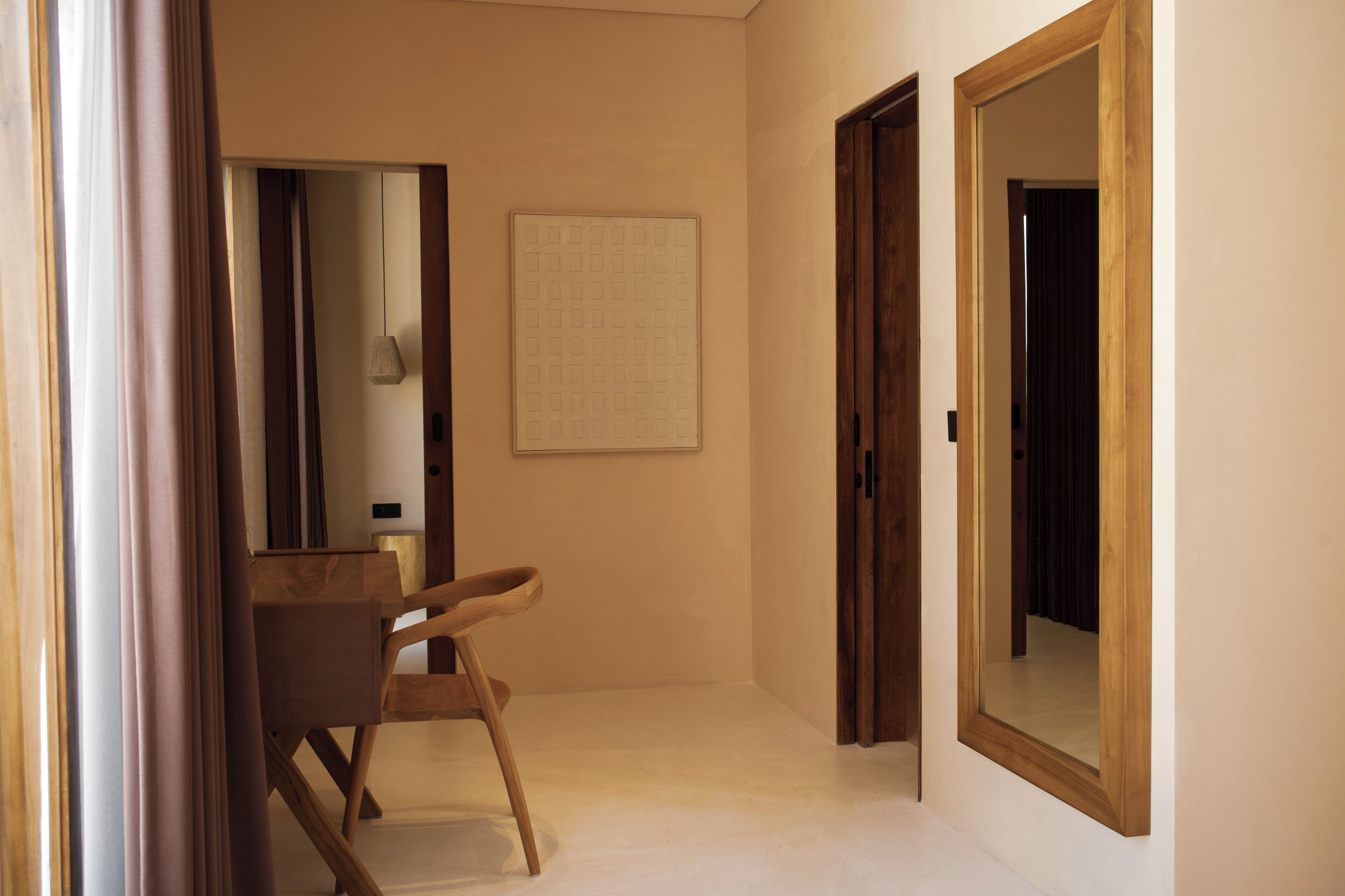 Un couloir avec une chaise en bois, un miroir et une porte donnant sur une autre pièce.