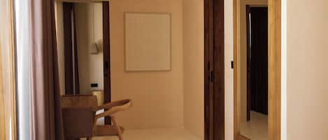 Un couloir avec une chaise en bois, un miroir et une porte donnant sur une autre pièce.
