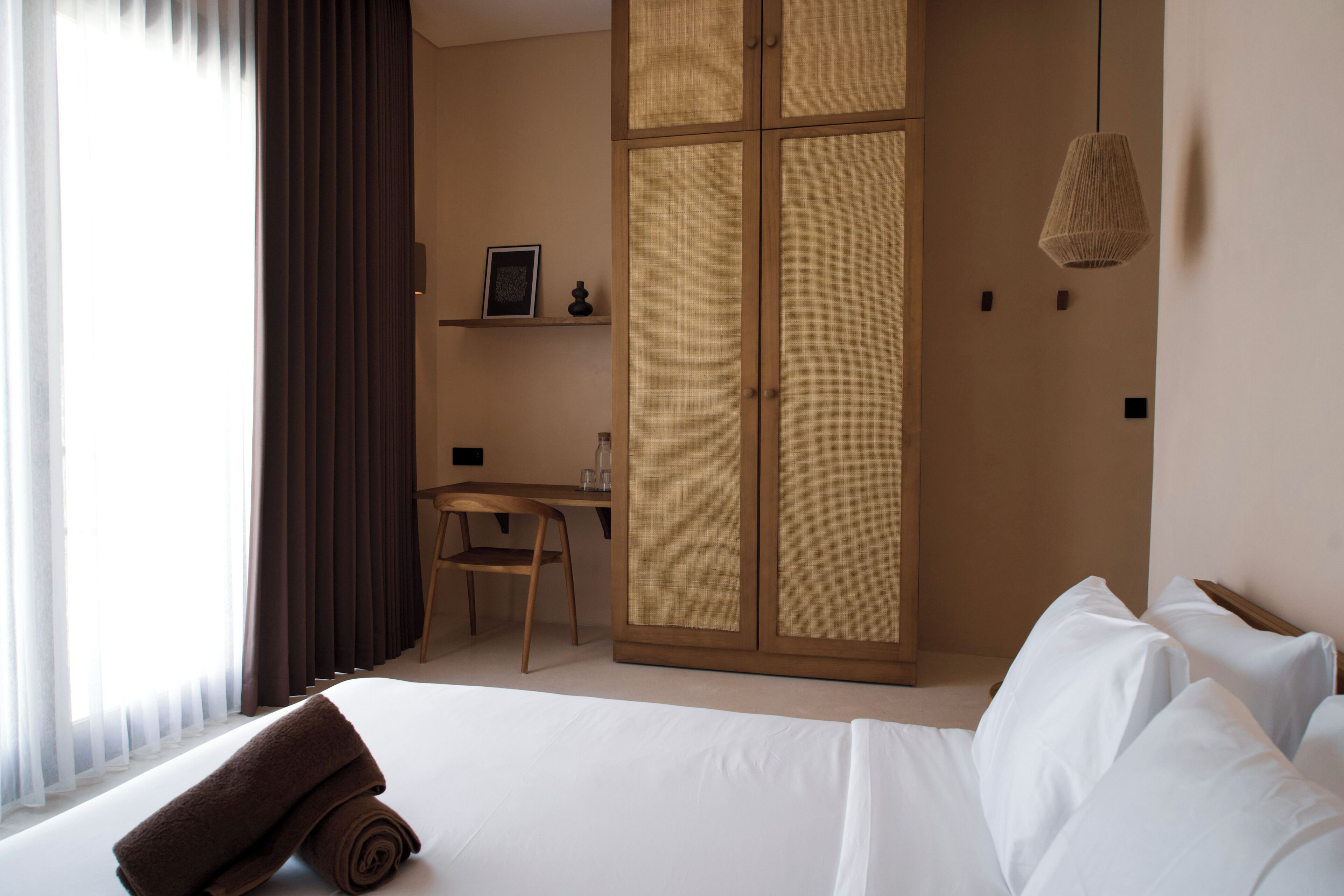 Une chambre d’hôtel comprenant un lit, un bureau, une chaise, une armoire et un luminaire suspendu.