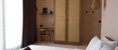 Habitación de hotel con cama, escritorio, silla, armario y lámpara colgante.