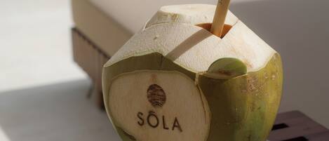 A coconut drink with a straw and the word 'SOLA' on a white plate.