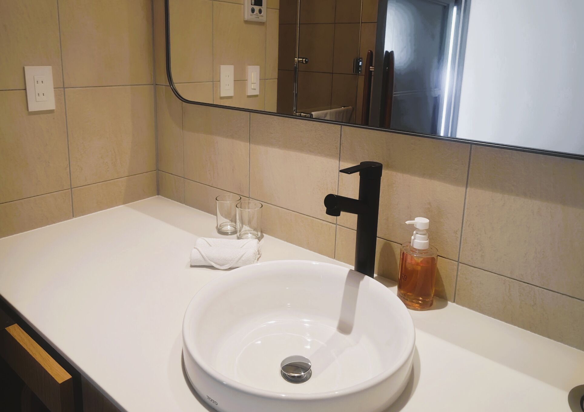 A bathroom with a white sink, a black faucet, and a mirror above it. There are two empty glasses and a bottle of soap on the sink.