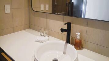 A bathroom with a white sink, a black faucet, and a mirror above it. There are two empty glasses and a bottle of soap on the sink.