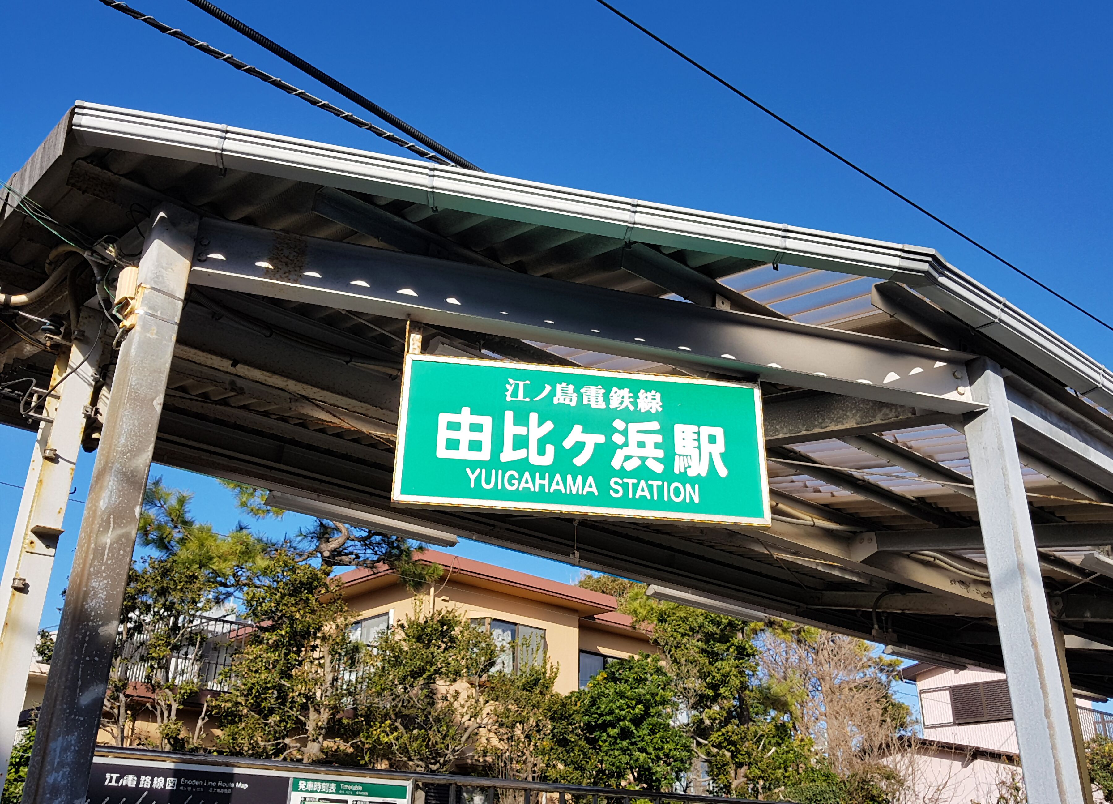 Señal de estación para Yuighama Station con un cielo despejado al fondo.