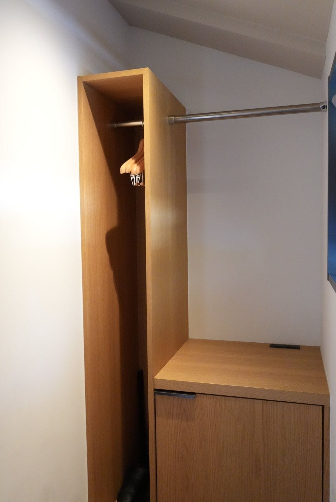 A compact room with a wooden wardrobe, a metal rod, and a small table.