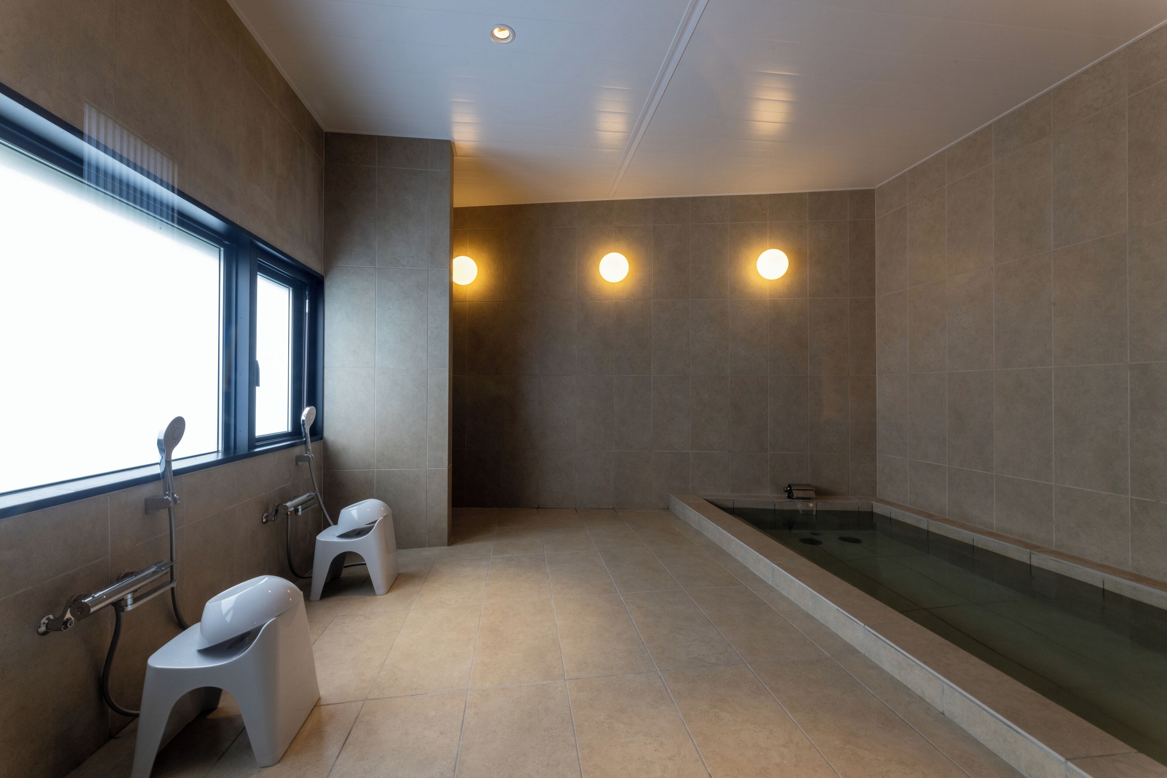 A modern bathroom with a bathtub, two toilets, and a window providing natural light.