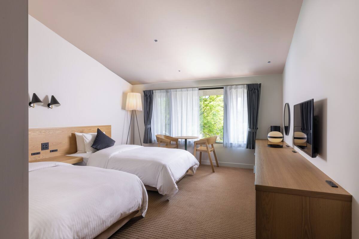 Hotellihuone, jossa on kaksi sänkyä, työpöytä, tuoli, televisio ja ikkuna, jossa on verhot.