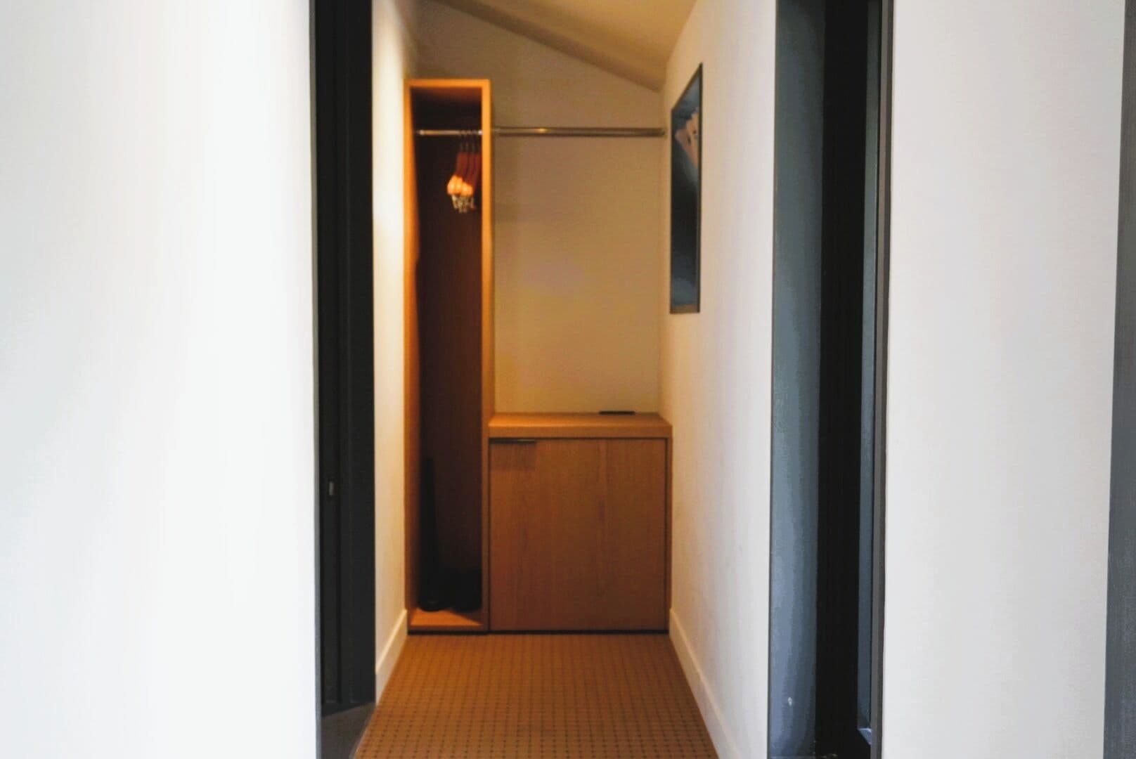 A narrow hallway with a wooden door at the end, a small shelf, and a framed picture on the wall.