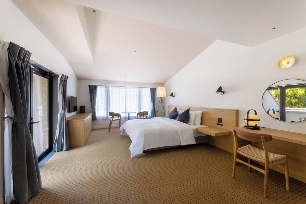 Hotellihuone, jossa on sänky, työpöytä, tuoli ja pieni pöytä tuoleineen.