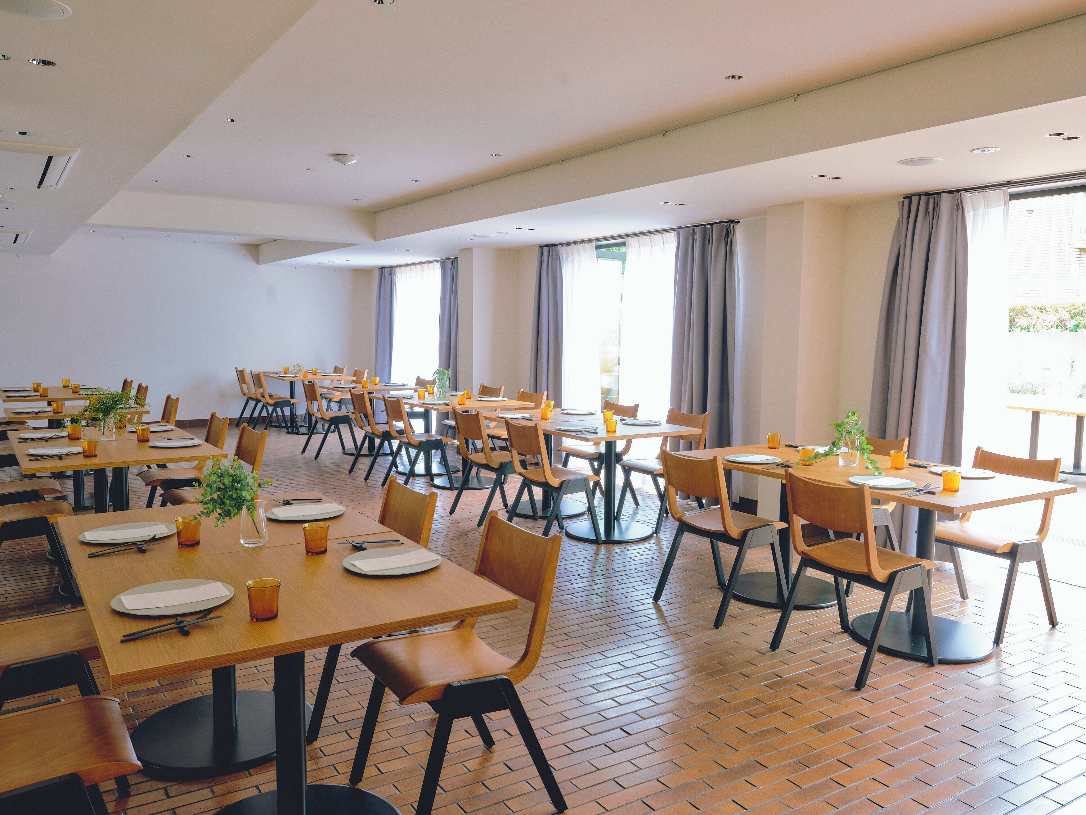 Un vaste espace dédié à la salle à manger, avec de nombreuses tables et chaises, de grandes fenêtres dotées de rideaux et un sol en briques.
