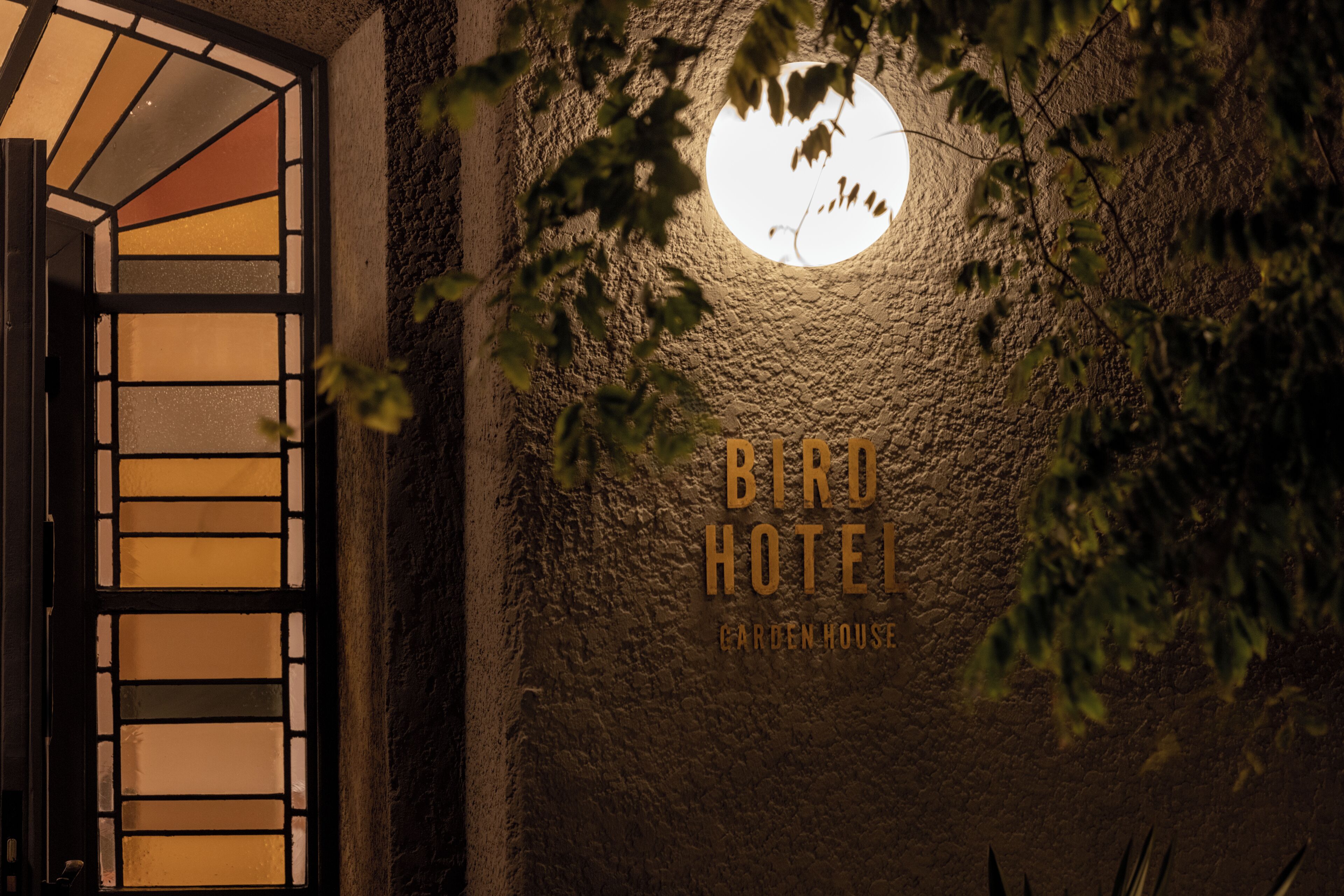 A textured wall with a circular window and the text "Bird Hotel Garden House".