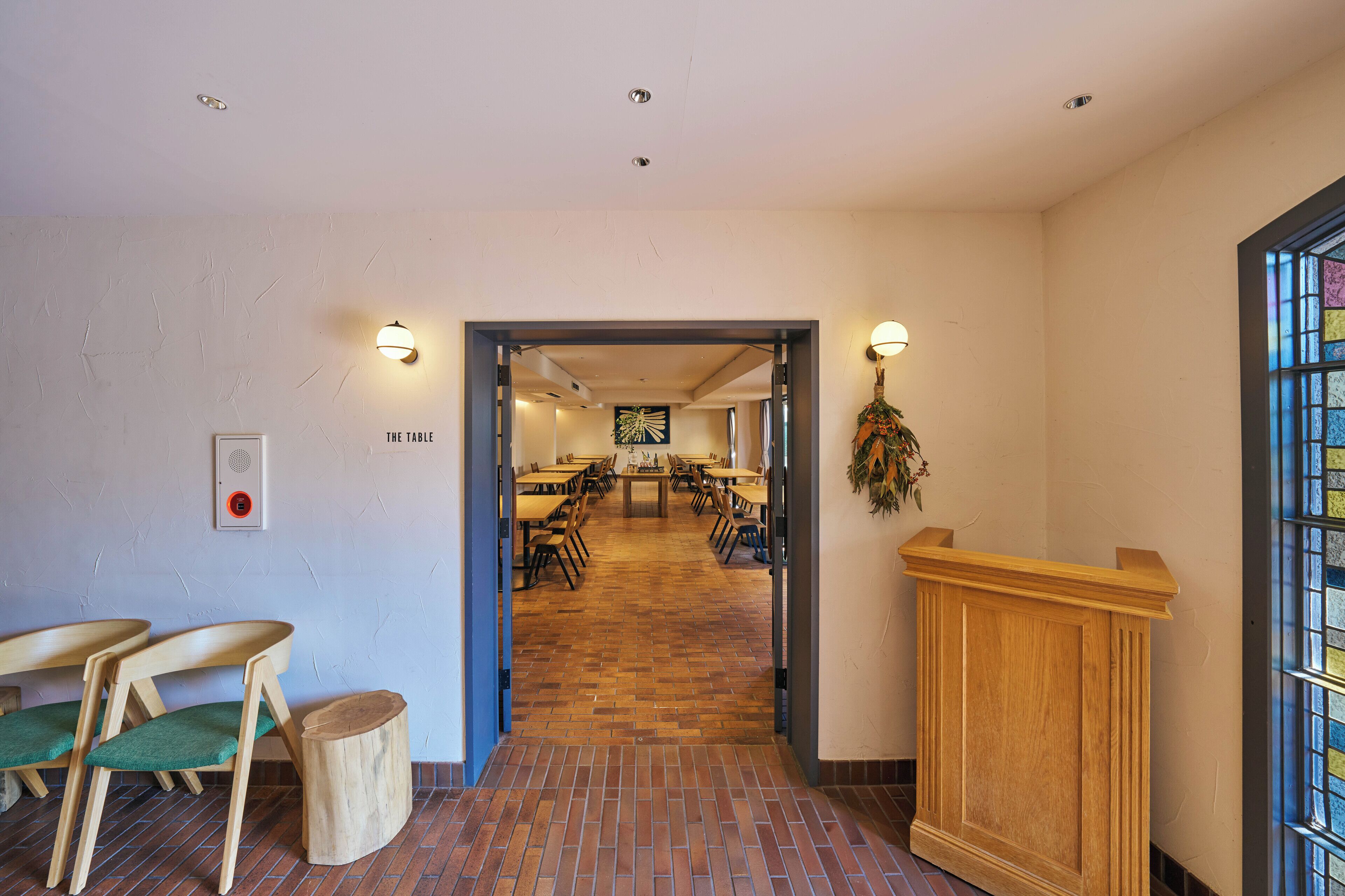 A hotel lobby with a brick floor, wooden chairs, a reception desk, and a view of the dining area.
