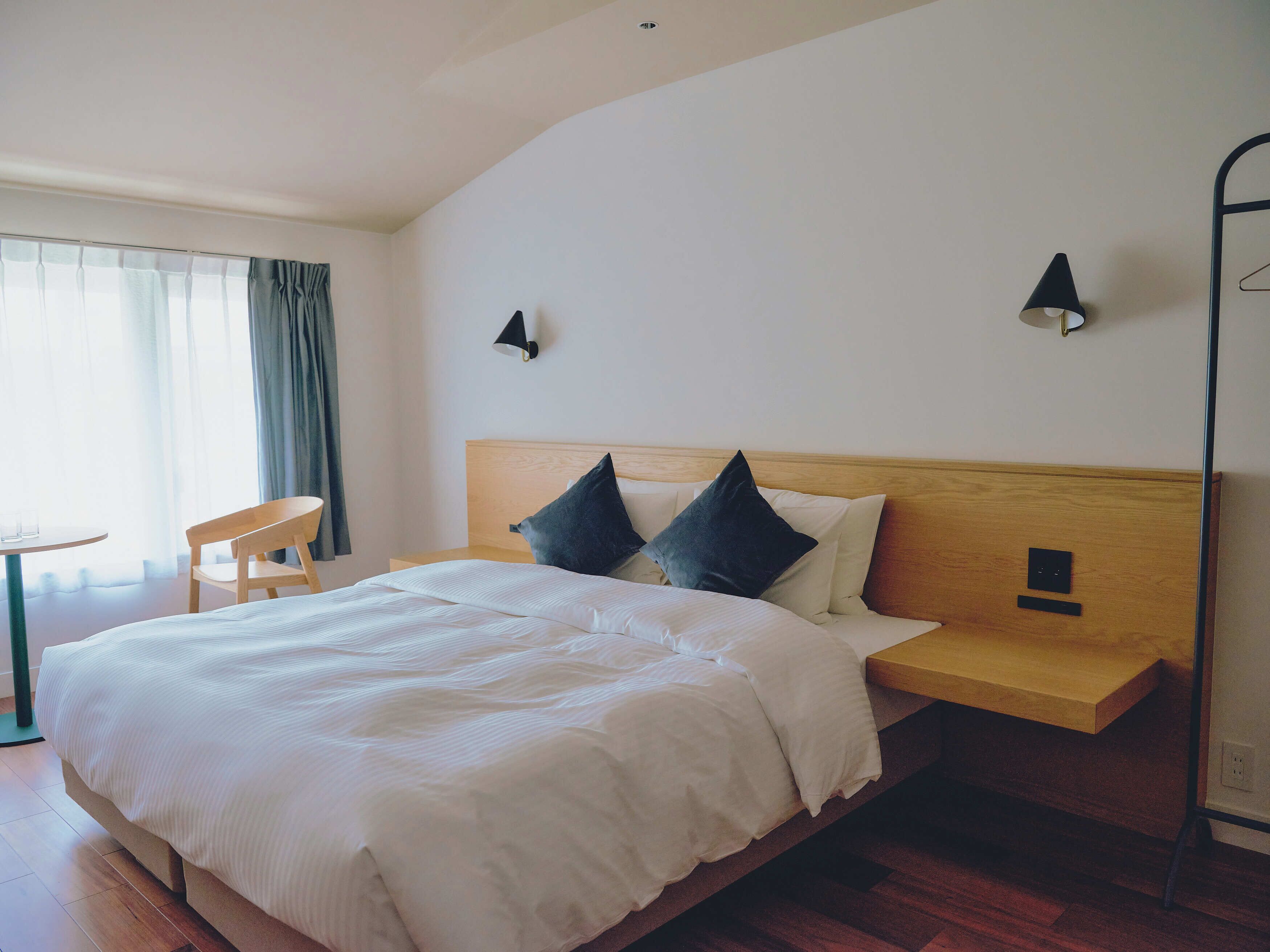 A neatly made bed with white linens, a wooden headboard, and two bedside lamps.
