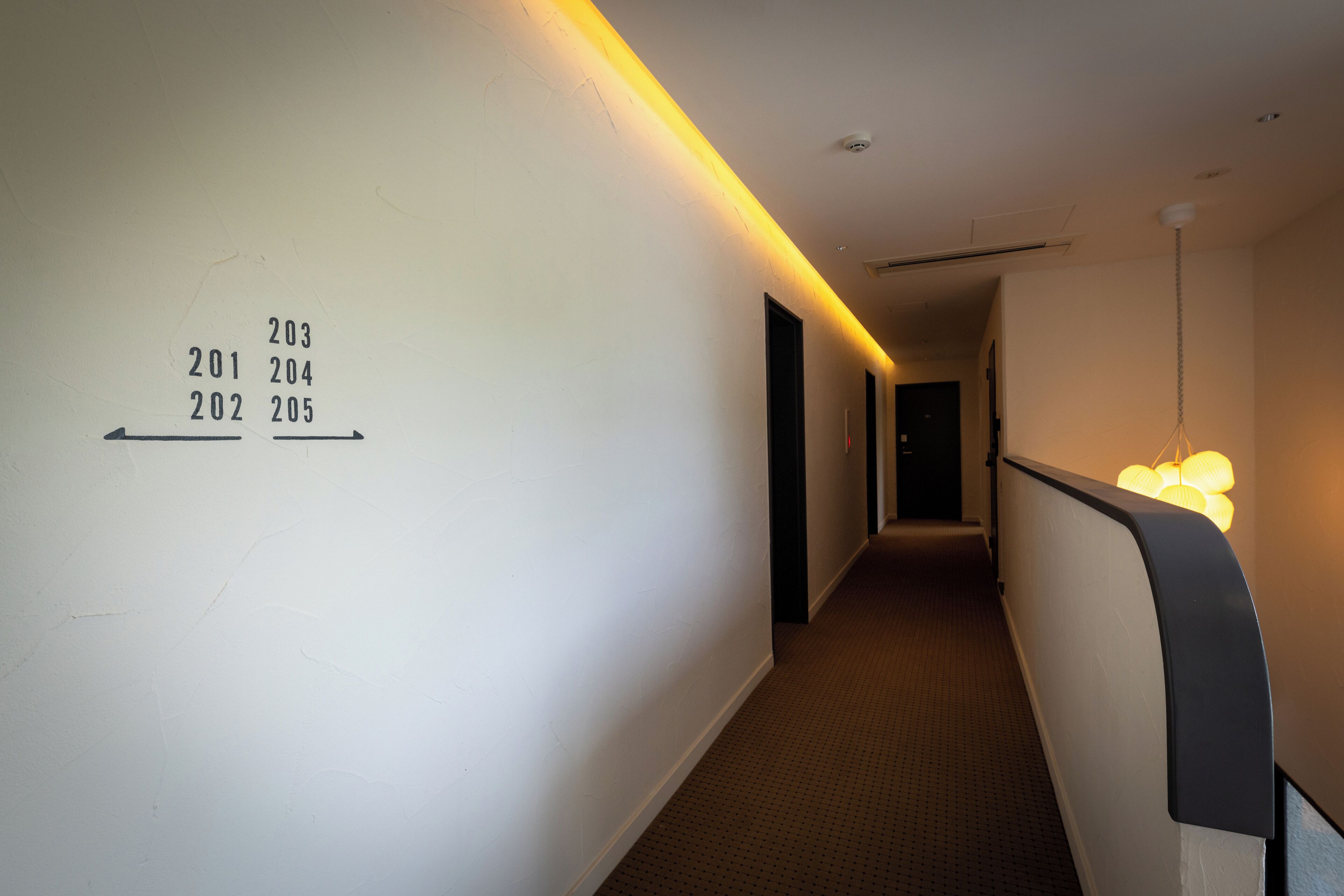 Un pasillo con puertas numeradas, piso alfombrado y un aplique en la pared.