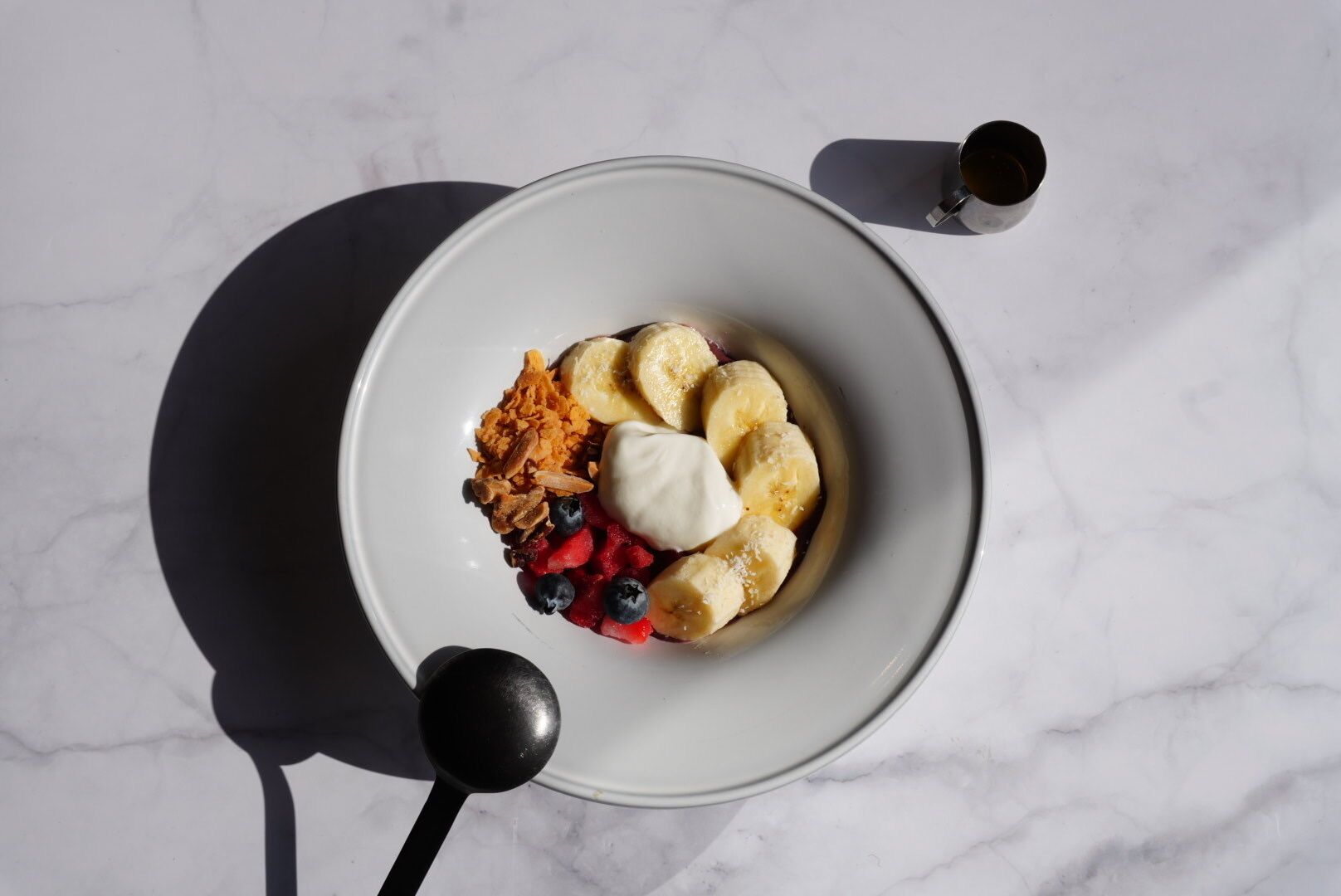 A bowl of food with bananas, berries, and a dollop of cream on a marble surface.