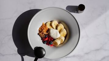 A bowl of food with bananas, berries, and a dollop of cream on a marble surface.