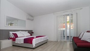 Une chambre d’hôtel moderne équipée d’un lit, d’un canapé, d’une table de chevet et d’une porte-fenêtre coulissante donnant sur le balcon.