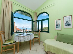 A room with a dining table set for two, two chairs, a green sofa, and two large windows with curtains. - Komfortable Ferienwohnung mit Balkon by Interhome (Makarska)