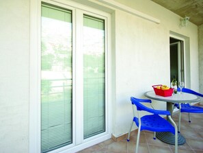A balcony with a round table, blue chairs, a red fruit basket, and a bottle of wine. - Große Wohnung in Zelenka mit Eigenem Parkplatz by Interhome (Makarska)