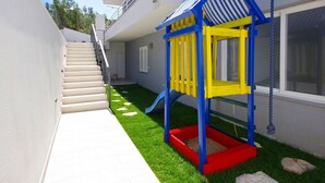 Una casa moderna con una escalera que lleva a un balcón, una zona de juegos con un tobogán y una ventana con vista al jardín.