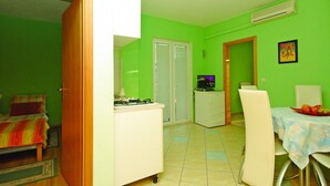 Una habitación compacta con una cama, una kitchenette pequeña, un comedor con mesa y sillas, y una puerta que da a otra habitación.