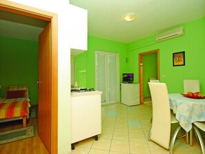 Ein kompaktes Zimmer mit Bett, einer kleinen Küchenzeile, einer Essecke mit Tisch und Stühlen sowie einer Tür zu einem weiteren Raum.