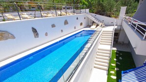 Una piscina con barrera de vidrio, zona de césped y una silla de descanso azul y amarilla.