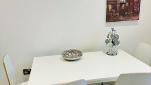 A dining area with a white table and chairs, a decorative bowl, and a wall-mounted painting. - Eurostar Comfort Inn Studio Apartments (London)