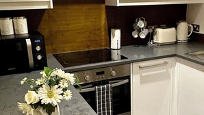 A modern kitchen with white cabinets, a black microwave, a stainless steel oven, a built-in dishwasher, and a granite countertop. - Eurostar Comfort Inn Studio Apartments (London)