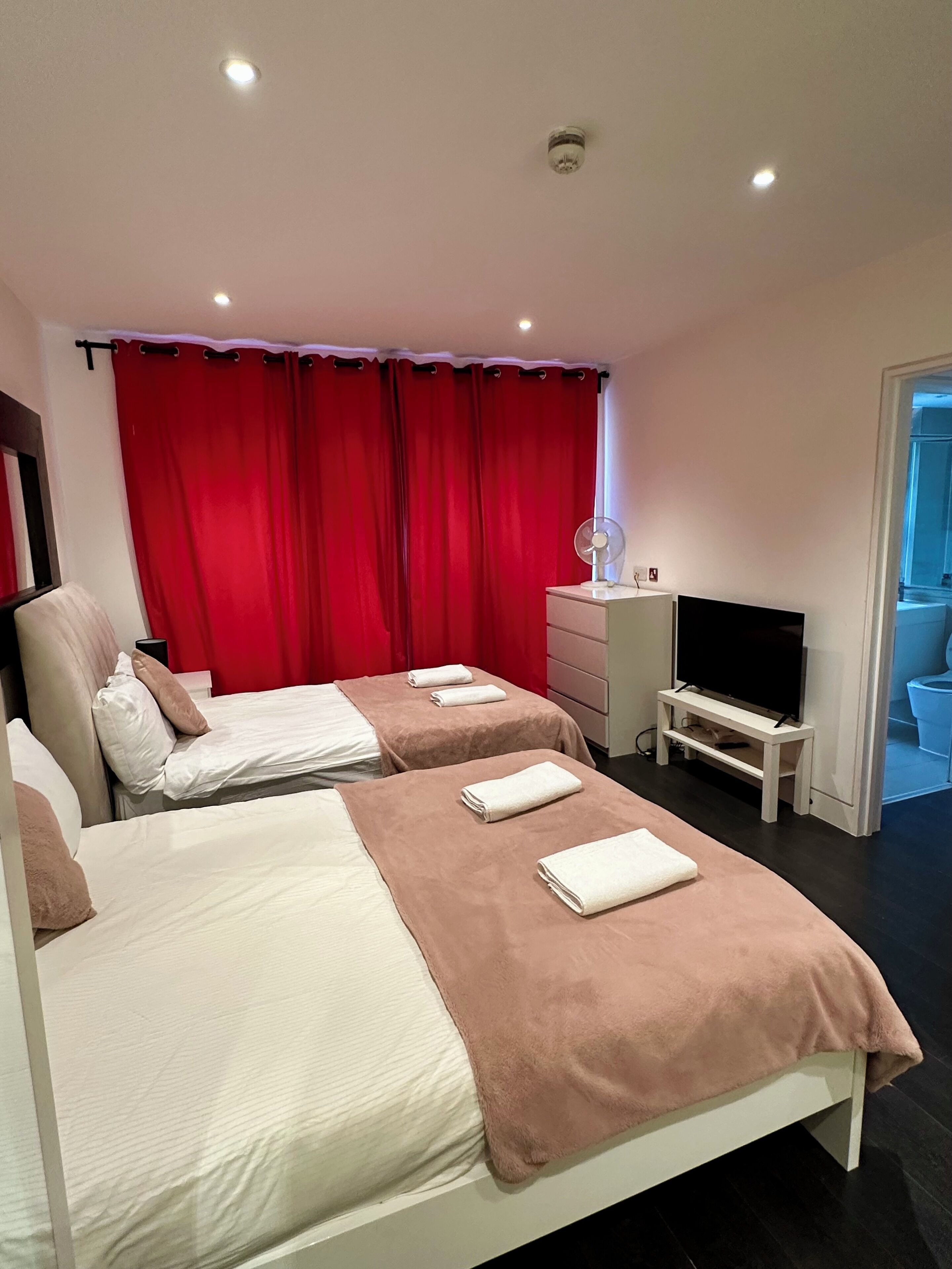 A hotel room with two beds, a TV, a fan, and a red curtain.