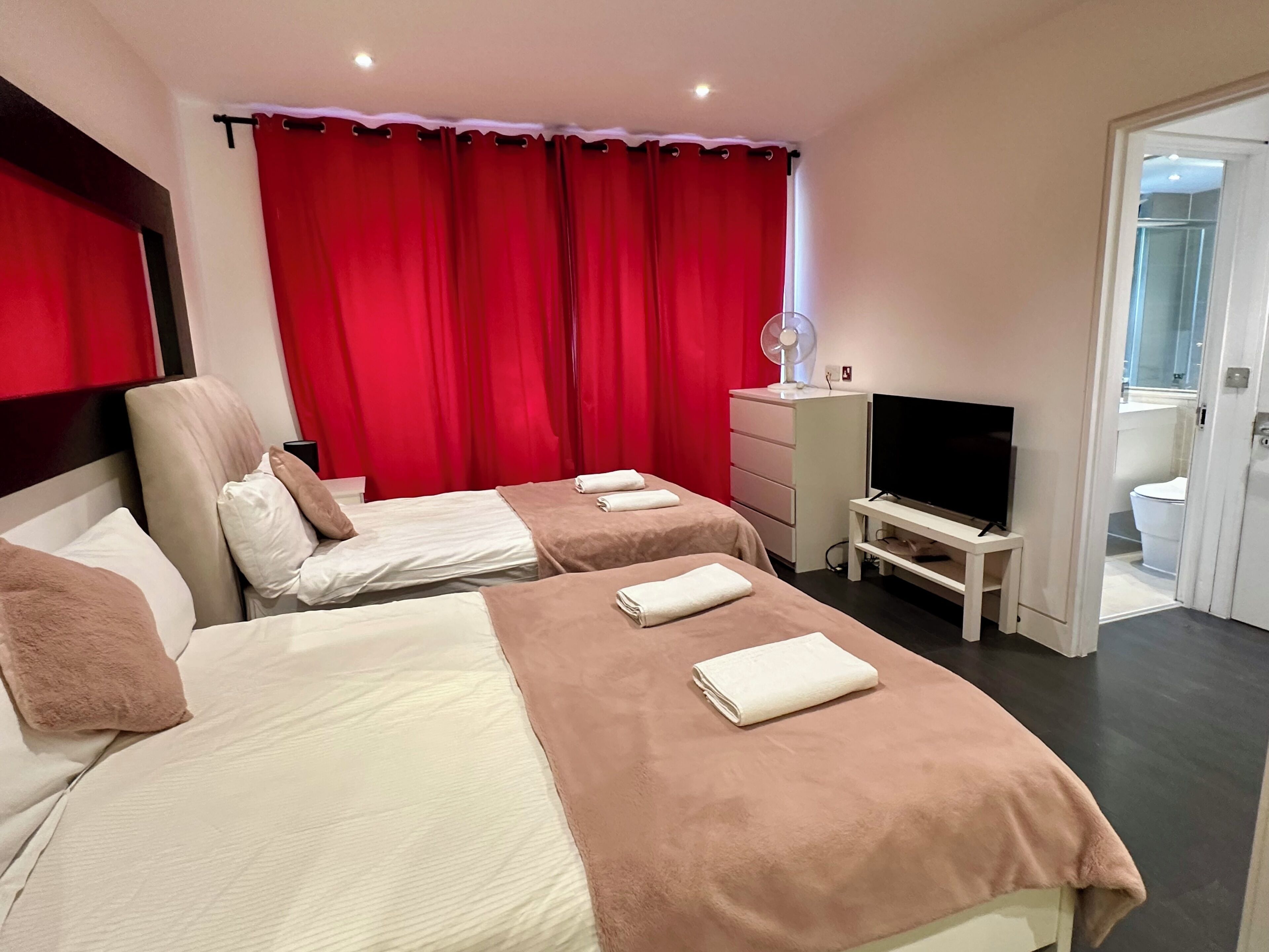 Habitación de hotel con dos camas, un televisor, un aparador y un baño visible a través de una puerta abierta.