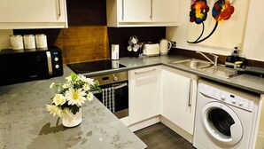 A compact kitchen with white cabinets, a built-in microwave, a toaster, and a washing machine. - Eurostar Comfort Inn Studio Apartments (London)