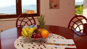Una mesa de comedor con frutero, sillas y vista al mar a través de amplios ventanales.