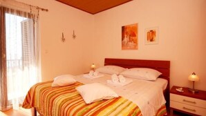 Un dormitorio con una cama, dos mesitas de noche, un ventanal con cortinas y dos luces fijadas a la pared.