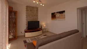 A living room with a flat-screen TV, a stone accent wall, a sofa, and a small side table. - Strandnahe Ferienwohnung in Podstrana by Interhome (Podstrana)