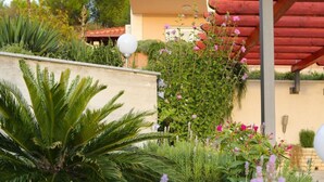 A garden with various plants and flowers, a red pergola, and a building with balconies in the background. - Strandnahe Ferienwohnung in Podstrana by Interhome (Podstrana)