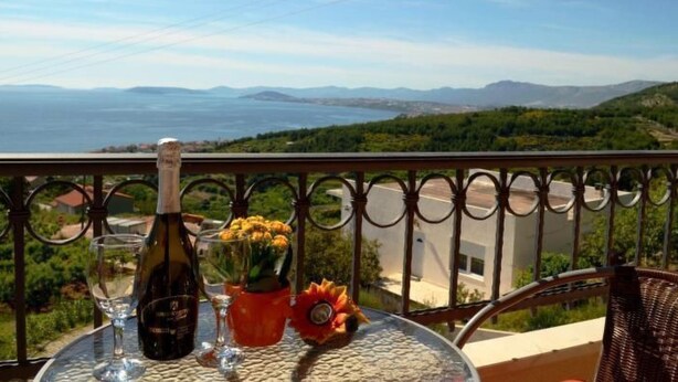 A table with a bottle of wine, a glass, and a flower arrangement on a balcony overlooking a scenic view. - Strandnahe Ferienwohnung in Podstrana by Interhome (Podstrana)