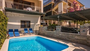 A swimming pool with lounge chairs, a stone wall, and a multi-story building with balconies. - Villa "Petra" mit Blick auf das Wasser by Interhome (Podstrana)