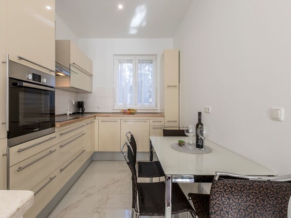 A modern kitchen with a Bosch oven, a dining table with chairs, and a window with curtains. - Villa Meri Split by Interhome (Dragovode)
