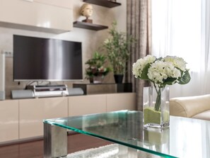 A modern living room with a glass coffee table, a flat-screen TV, a vase with white flowers, and a sofa. - Villa Meri Split by Interhome (Dragovode)