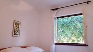 Ein Schlafzimmer mit Bett, Fenster mit Blick auf Bäume und einem gerahmten Bild an der Wand.