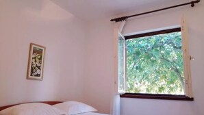 Ein Schlafzimmer mit einem Bett, einem Fenster mit Blick auf Bäume und einem gerahmten Bild an der Wand.