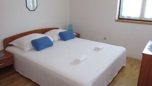 Una cama bien tendida con almohadas blancas y azules, un cabecero de madera y una mesita de noche con una lámpara.