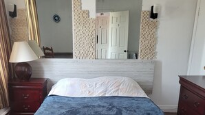 A bedroom with a bed, a nightstand, a lamp, a dresser, and a mirror.
