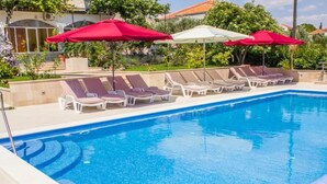 Ein Swimmingpool mit Liegestühlen und Sonnenschirmen, umgeben von Grünflächen und Gebäuden.